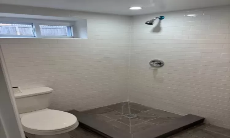 Bathroom with toilet, tile patterned flooring, a tile shower, and tile walls