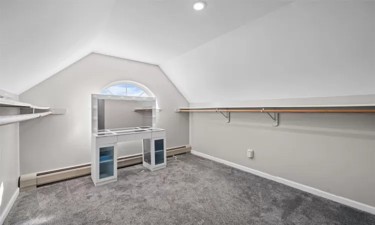 Spacious closet with carpet floors, lofted ceiling, and baseboard heating