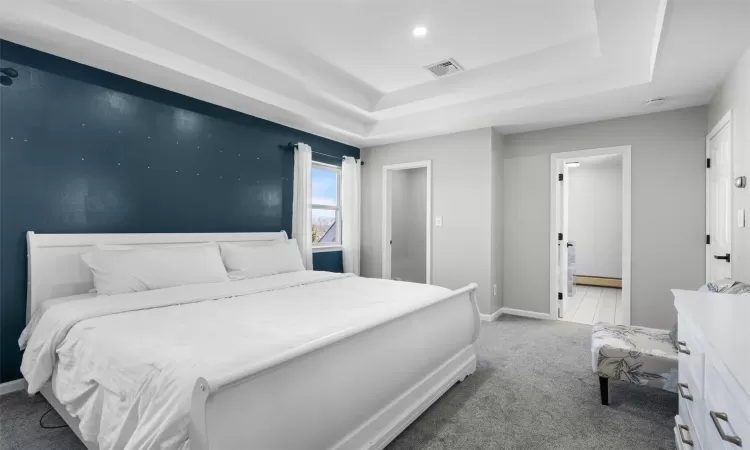 Bedroom featuring baseboards, visible vents, ensuite bath, carpet, and a tray ceiling