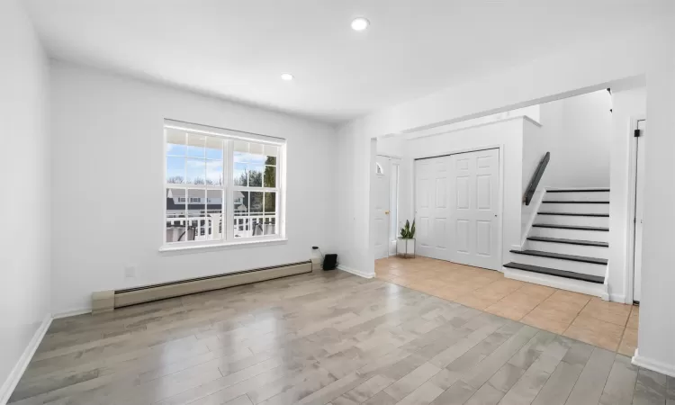 Entryway with a baseboard radiator, recessed lighting, wood finished floors, baseboards, and stairway