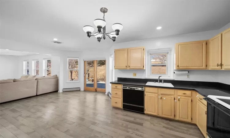 Kitchen with dark countertops, baseboard heating, light brown cabinets, a sink, and dishwasher