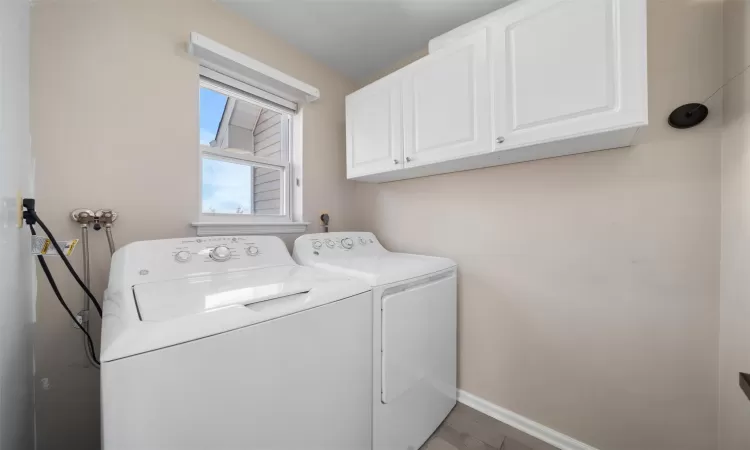 Washroom featuring washer and clothes dryer, wood finished floors, cabinet space, and baseboards