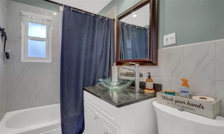 Bathroom featuring toilet, shower / tub combo, vanity, and tile walls