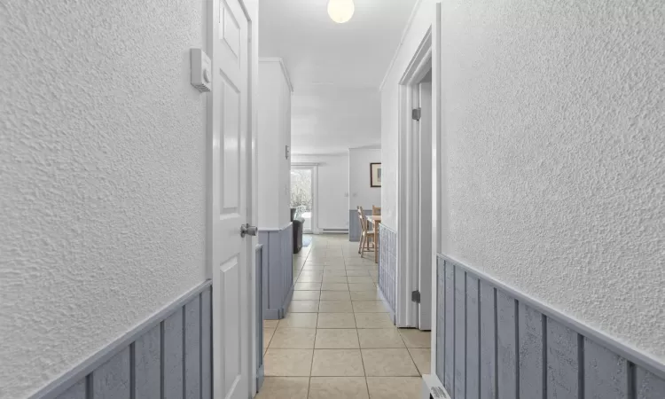 Hall featuring light tile patterned floors, a wainscoted wall, and a textured wall