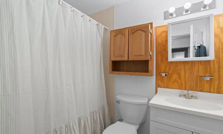 Full bathroom featuring curtained shower, a textured wall, toilet, vanity, and a textured ceiling