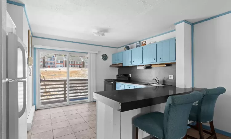 Kitchen featuring blue cabinets, a sink, electric stove, freestanding refrigerator, and dark countertops