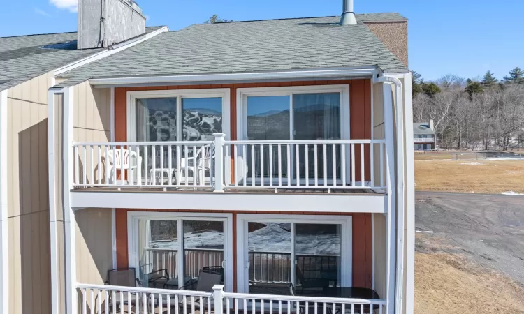 Rear view of house featuring roof with shingles, a chimney, and a balcony