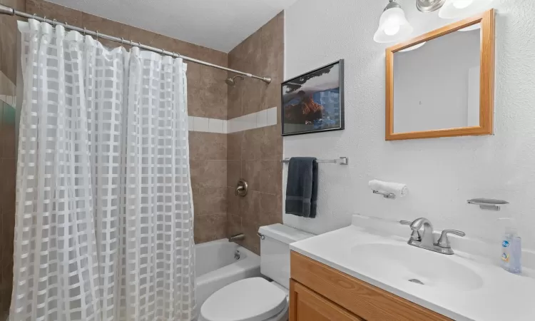 Bathroom featuring a textured wall, toilet, shower / bath combo, vanity, and a textured ceiling