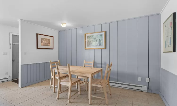 Dining space featuring light tile patterned floors, a baseboard radiator, and crown molding