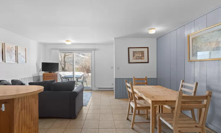 Dining space featuring a wainscoted wall, a baseboard radiator, ornamental molding, and light tile patterned flooring