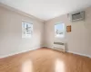 Unfurnished room featuring light wood finished floors, a wall mounted air conditioner, a wealth of natural light, and radiator