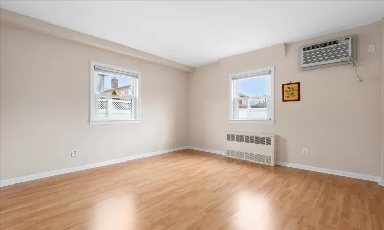 Unfurnished room featuring light wood finished floors, a wall mounted air conditioner, a wealth of natural light, and radiator