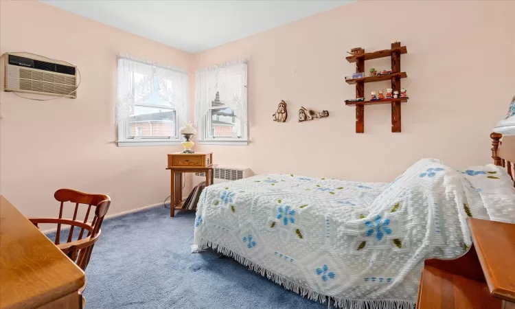 Bedroom featuring a wall unit AC, radiator, baseboards, and carpet flooring