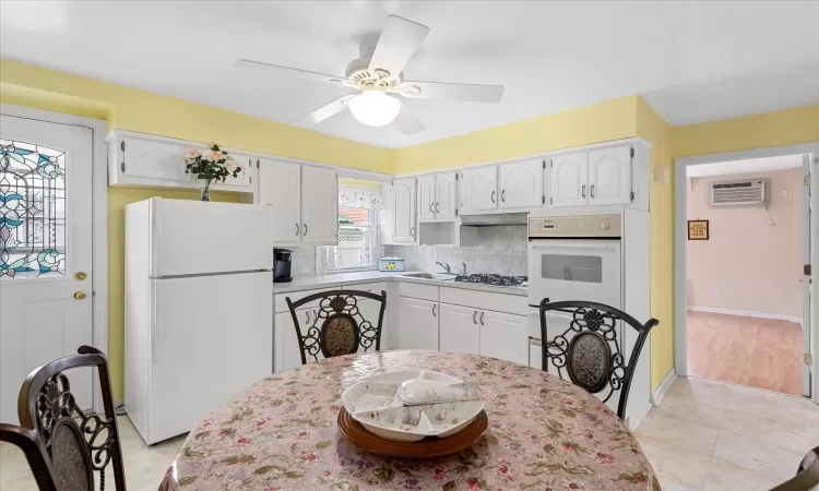 Kitchen featuring white appliances, a ceiling fan, white cabinets, a wall mounted AC, and backsplash