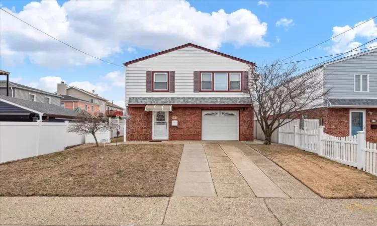 View of front of property with brick siding, roof with shingles, concrete driveway, an attached garage, and fence