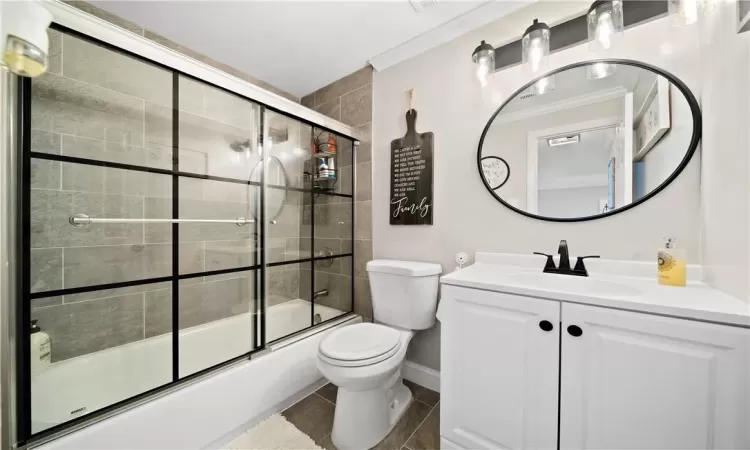 Full bathroom with tile patterned floors, enclosed tub / shower combo, ornamental molding, vanity, and toilet