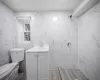 Bathroom with toilet, a tile shower, tile walls, and vanity