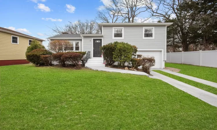 Split level home with an attached garage, fence, driveway, and a front lawn