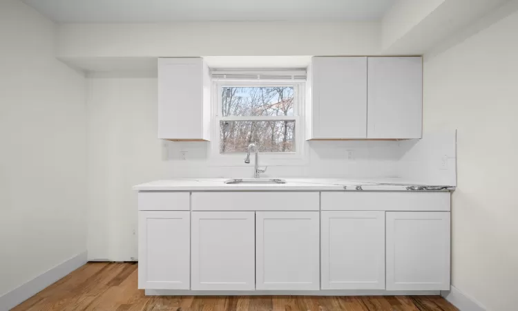 Kitchen with light countertops, light wood-type flooring, a sink, and white cabinets