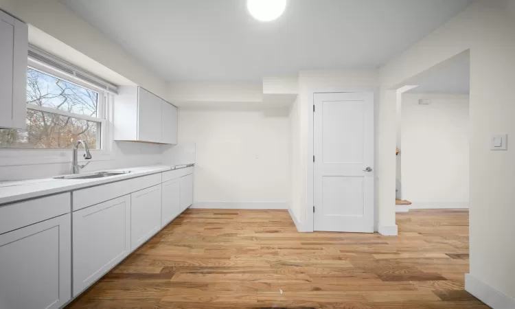 Kitchen featuring light countertops, a sink, light wood-style flooring, and baseboards