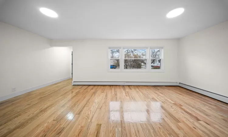 Unfurnished room with a baseboard radiator, baseboards, and wood finished floors