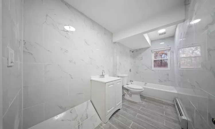 Bathroom featuring shower / bathtub combination, toilet, vanity, tile walls, and baseboard heating