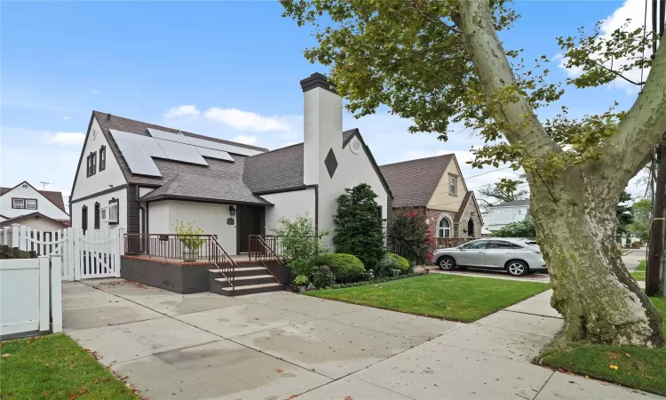 View of front of property with a chimney, roof with shingles, a gate, roof mounted solar panels, and stucco siding