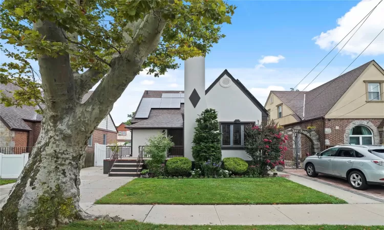 View of front of home with solar panels, stucco siding, a gate, fence, and a front yard