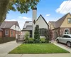 Tudor home with solar panels, stucco siding, a chimney, fence, and a front yard