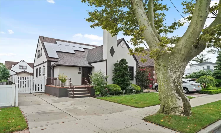 View of front facade with stucco siding, a shingled roof, a gate, roof mounted solar panels, and fence