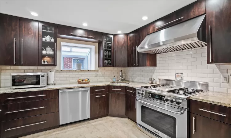 Kitchen with stainless steel appliances, a sink, light stone counters, and extractor fan