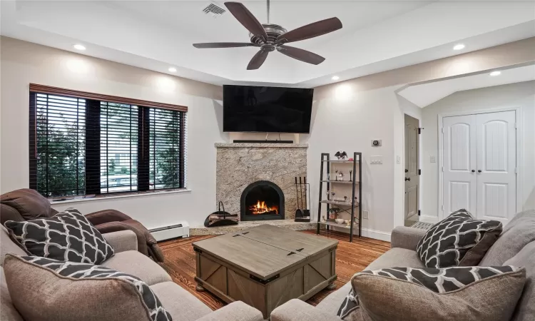 Living area featuring a warm lit fireplace, a baseboard radiator, recessed lighting, wood finished floors, and visible vents