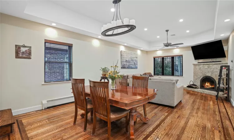 Dining room featuring a baseboard heating unit, a tray ceiling, a stone fireplace, and wood finished floors