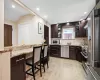 Kitchen with dark brown cabinetry, under cabinet range hood, stainless steel appliances, backsplash, and glass insert cabinets