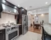 Kitchen featuring light stone counters, dark brown cabinetry, visible vents, high quality appliances, and wall chimney exhaust hood