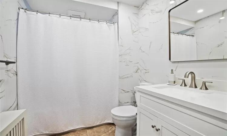 Full bathroom with toilet, curtained shower, tile walls, and vanity