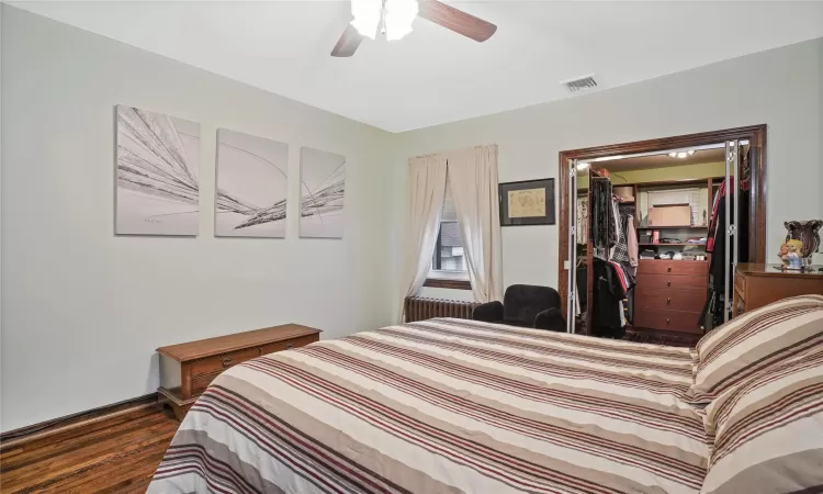 Bedroom with wood finished floors, a ceiling fan, baseboards, visible vents, and radiator