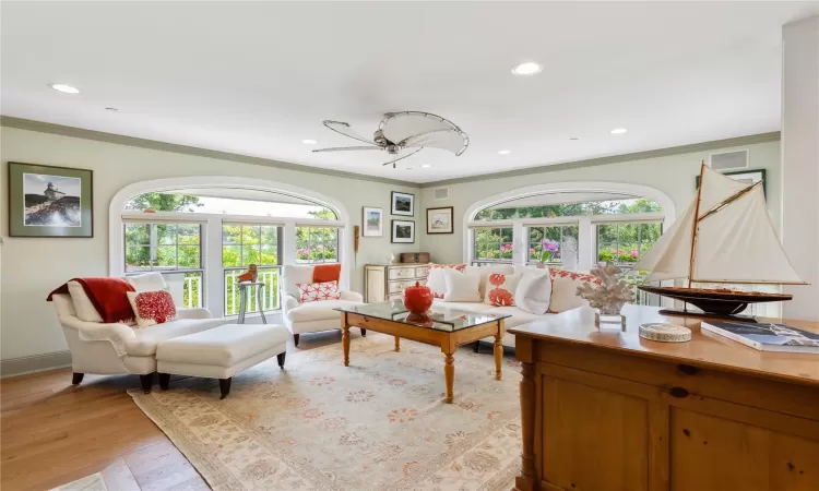 Professional appointed living area featuring ornamental crown and base moulding, recessed lighting, light wood-type flooring, and plenty of natural light.