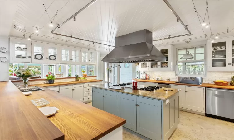 Kitchen with Antique Heart Pine countertops imported from a restored barn in Pennsylvania.  Tile backsplash,  stainless steel dishwasher, white cabinetry, and stainless steel exhaust range hood