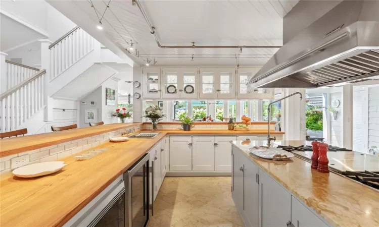 Kitchen with exposed track lighting system, double sided glass door hanging cabinets cabinets, wood counters, wine cooler, and extractor fan