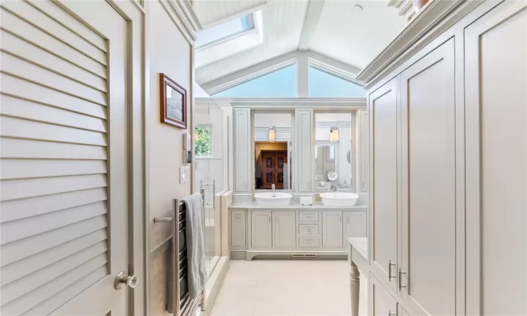 Full bathroom featuring lofted ceiling with skylight, dual vanity sink, custom cabinetry and trim work, and radiant heat floors