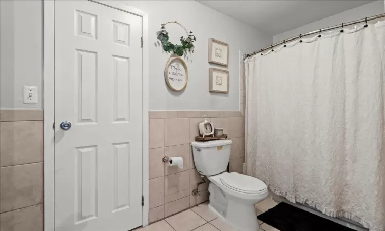 Bathroom featuring tile patterned flooring, wainscoting, tile walls, and toilet