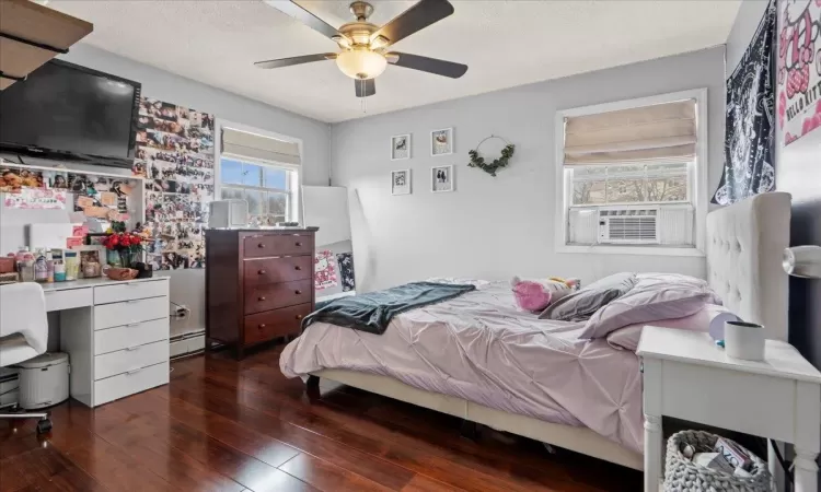 Bedroom featuring a textured ceiling, cooling unit, a baseboard heating unit, a ceiling fan, and dark wood-style floors