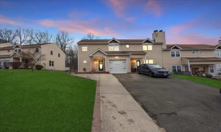 Townhome / multi-family property with driveway, an attached garage, and a lawn