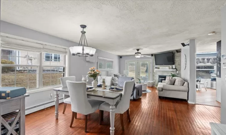 Dining room with dark wood finished floors, a fireplace, baseboard heating, a textured ceiling, and ceiling fan with notable chandelier