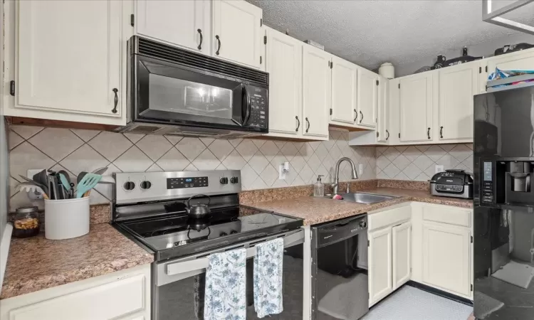 Kitchen featuring a textured ceiling, a sink, light countertops, black appliances, and tasteful backsplash