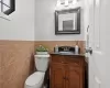 Bathroom featuring toilet, wainscoting, vanity, and tile walls