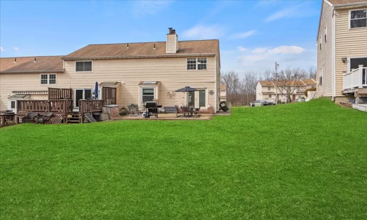 Back of house featuring a deck, a patio, a chimney, and a lawn