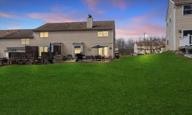 Back of property at dusk featuring a patio area, a chimney, a lawn, and a wooden deck