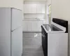 Kitchen with electric range, white cabinetry, a sink, and freestanding refrigerator